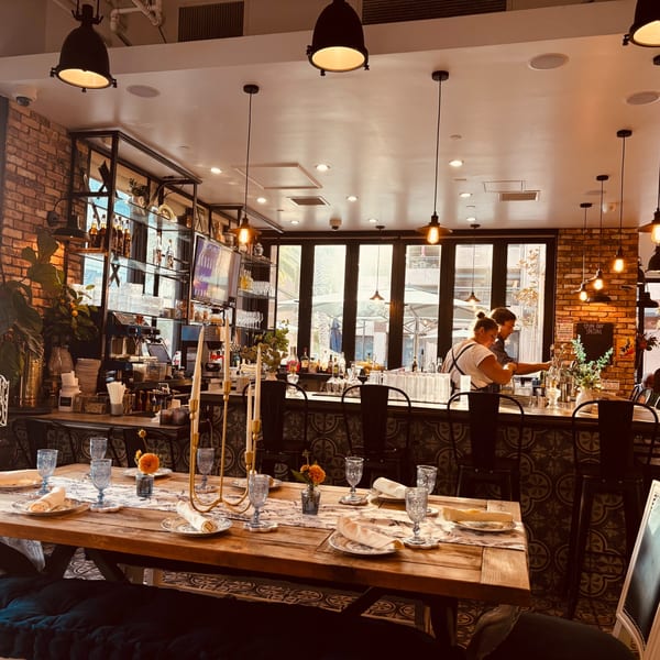 Maldon's Brasserie interior with a set dining table in the foreground and a bar with staff.