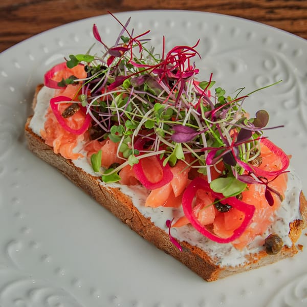 Smoked salmon toast with cream cheese, pickled onions, capers, and microgreens on a white plate.