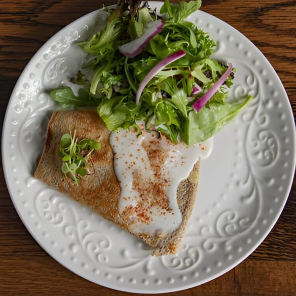 A savory crepe with white sauce and spices, served with a fresh green salad on a white plate.
