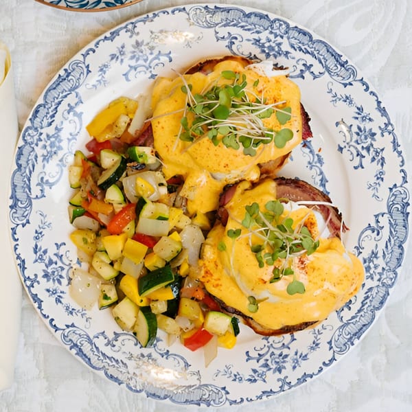Eggs Benedict with hollandaise sauce and microgreens, served with a side of roasted vegetables.