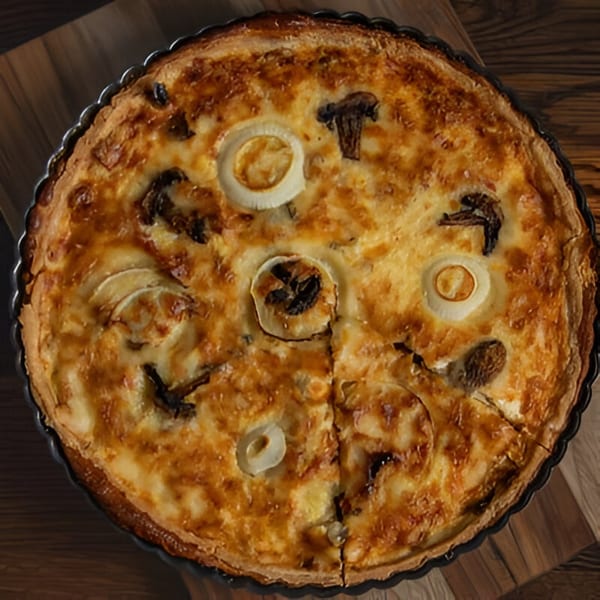 Overhead view of a golden-brown French quiche with mushroom and onion slices, one piece removed.